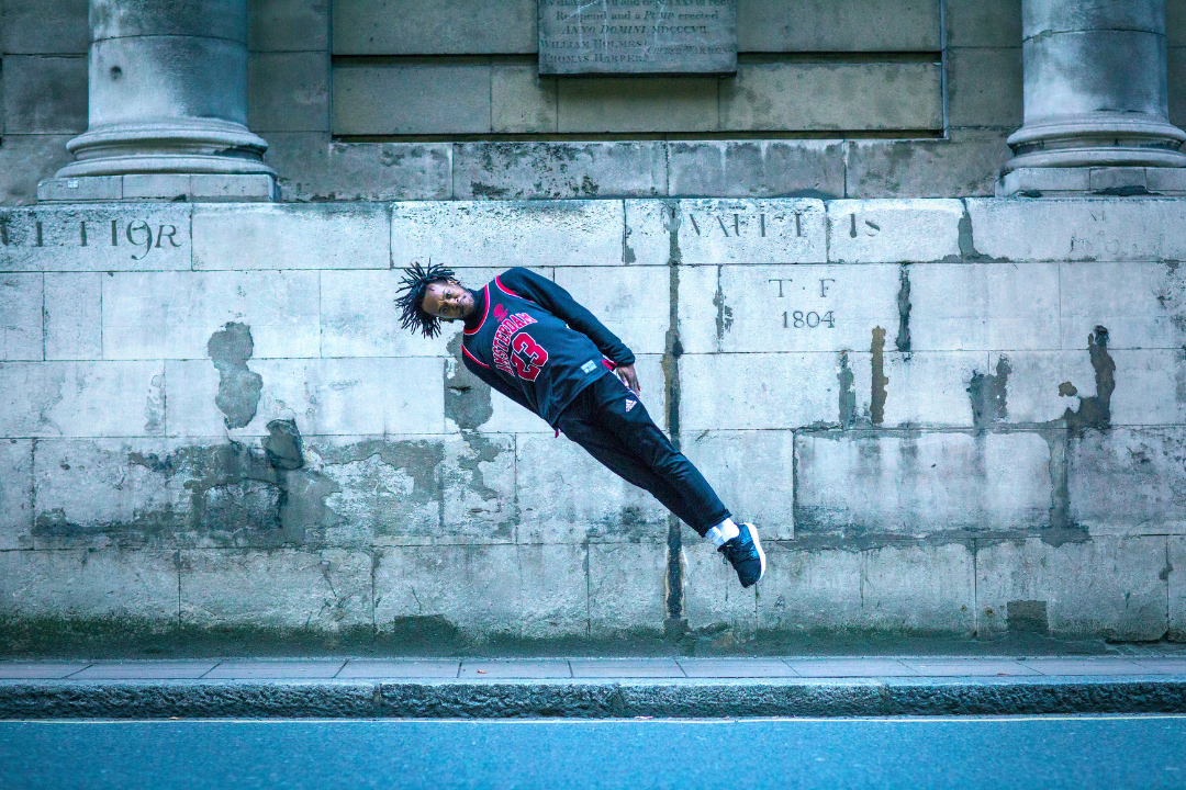 Dancer jumping in mid-air on a London street with their arms by their side, pointing their body at an angle.