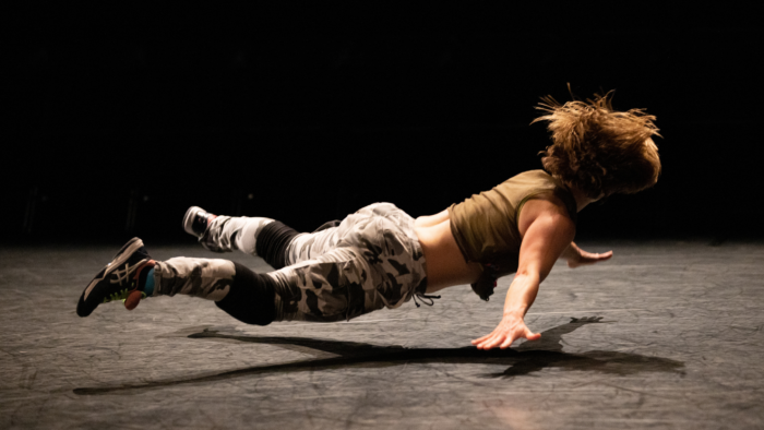 A dancer falling face down with their arms and legs spread out, hovering just above the stage.