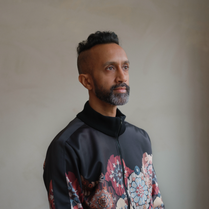 Portrait of Hetain Patel wearing a black bomber jacket with carpet patterns