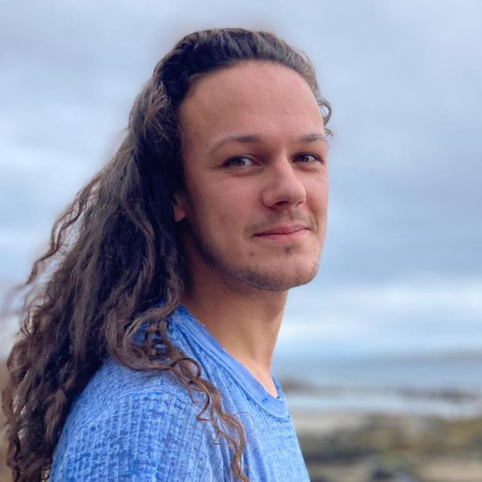 Portrait of Tom Cassani at the beach, wearing a blue knit jumper