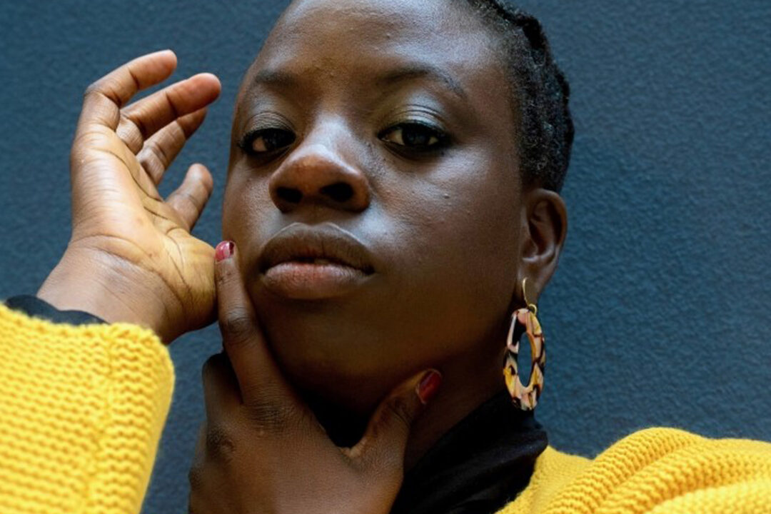 Portait of Anthea Lewis, a Black woman with gold earrings and a bright yellow jumper