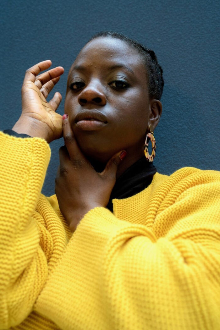 Portait of Anthea Lewis, a Black woman with gold earrings and a bright yellow jumper