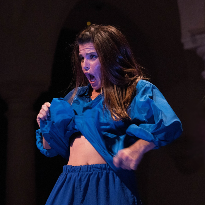 A performer in a blue two-piece tracksuit is passionately dancing, showcasing her movement and expression, slightly lifting up her jacket to show her midriff.